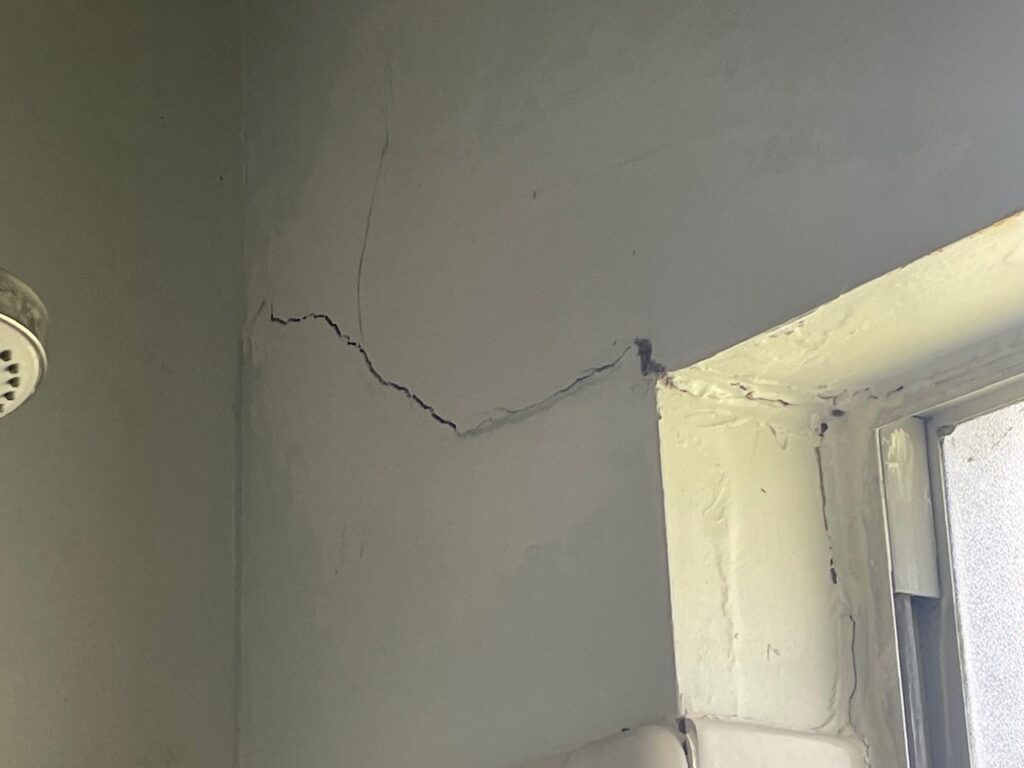 Visible structural diagonal cracking is seen at the corners of windows and along the middle of ceilings in the home.